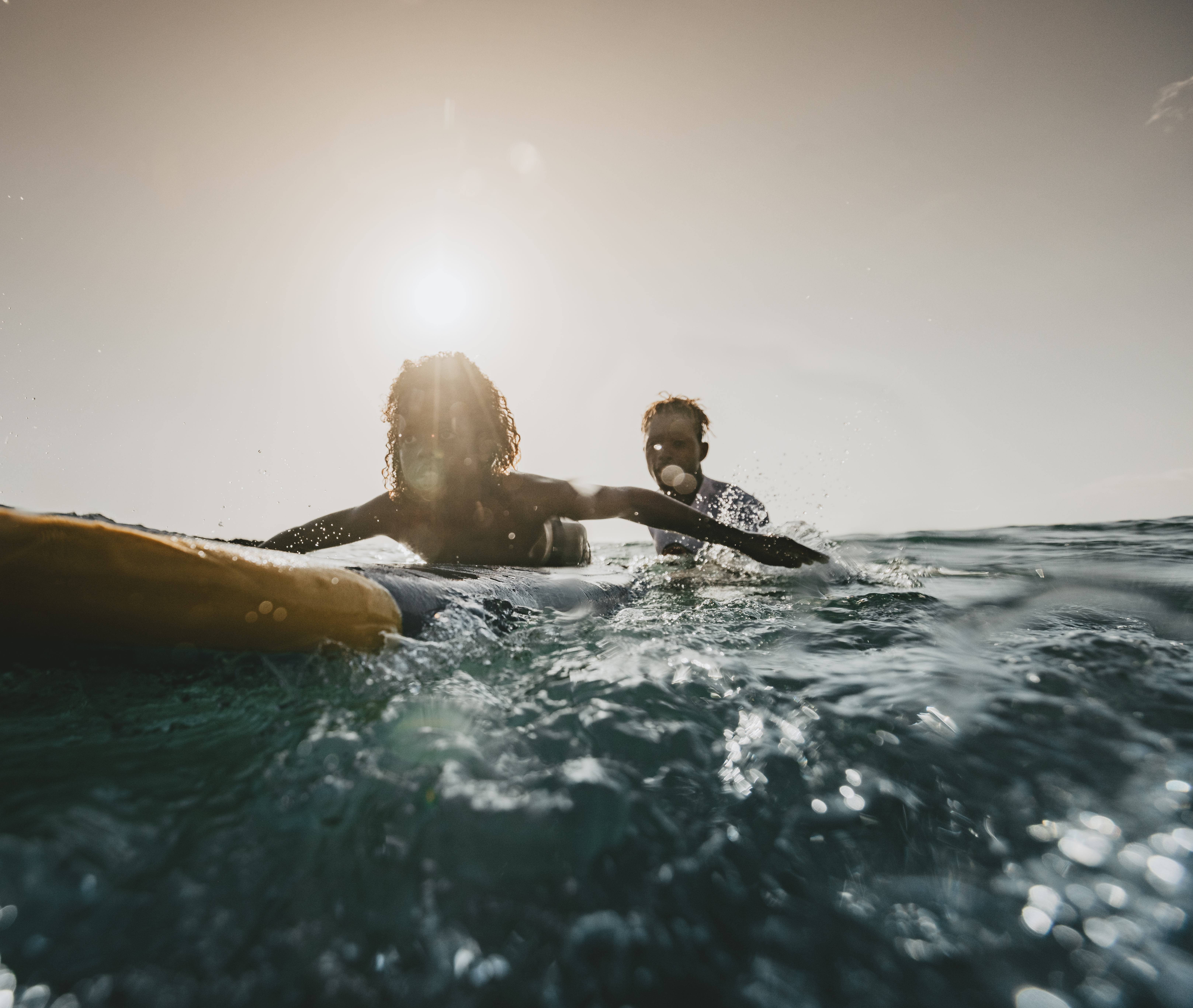 Two surfers paddling at sunset